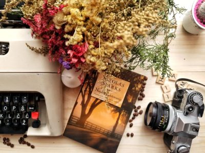 bunch of flowers and book arranged on wooden table with vintage typewriter and camera