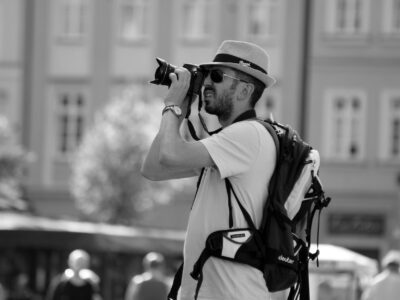 man in hat and sunglasses taking pictures with camera on city square