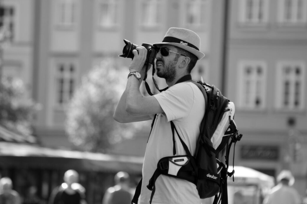 man in hat and sunglasses taking pictures with camera on city square