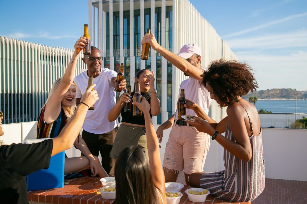 joyful diverse friends toasting with beer bottles on rooftop